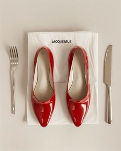 a pair of red high heels sitting on top of a napkin next to a fork and knife