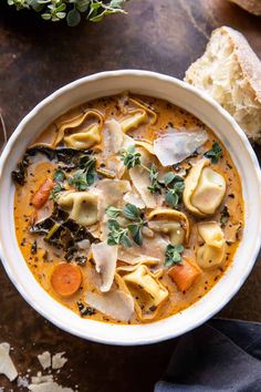 a white bowl filled with tortellini soup on top of a wooden table next to a piece of bread