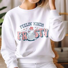 Chase the winter blues away and bring some festive fun to your wardrobe with the Feelin' Kinda Frosty Funny Snowman Winter Sweatshirt. This whimsical graphic sweatshirt features a smiling snowman and playful text that will put a smile on your face all season long. Show off your playful spirit and get in the festive mood with this retro-inspired snowman design. The smiling snowman graphic paired with the cheeky text adds a dose of lighthearted charm that's perfect for the holidays and snow days alike. Funny Print Long Sleeve T-shirt For Winter, Funny Print Winter Sweatshirt, Funny Print Sweatshirt For Winter, Winter Fun Relaxed Fit Tops, Fun Winter Tops With Relaxed Fit, Winter Funny Print Crew Neck Top, Winter Crew Neck Top With Funny Print, Fun Winter Sweatshirt With Letter Print, Fun Crew Neck Winter Tops