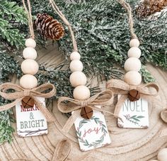 three wooden ornaments hanging from twine with christmas decorations around them and pine cones in the background