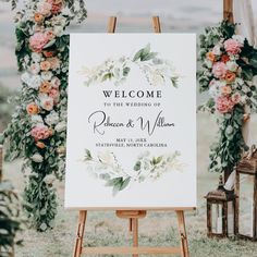 an easel with a welcome sign on it and flowers in the background for a wedding ceremony