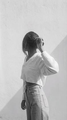 a woman standing in front of a white wall talking on a cell phone