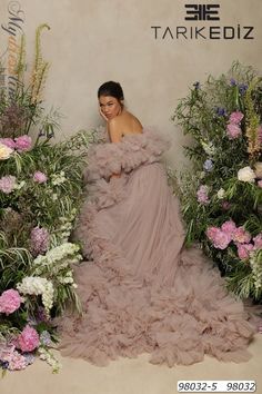 a woman is standing in front of flowers wearing a dress with ruffles on it