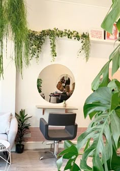 a mirror sitting above a hair dresser in a room with lots of greenery on the walls