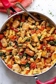 a skillet filled with pasta and vegetables on a white counter top next to a red towel