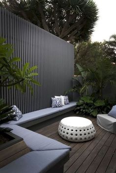 an outdoor seating area with white cushions and plants on the side walk, next to a wooden deck