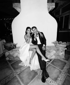 a man and woman are sitting on a stone bench in front of a white wall