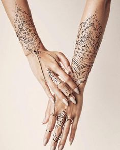 two hands holding each other with henna tattoos on their arm and hand, both covered in intricate designs