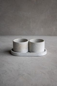 two white cups sitting on top of each other in front of a gray wall and floor