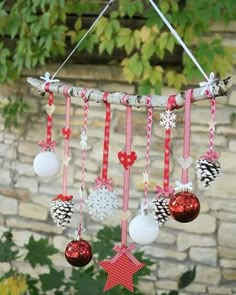 christmas ornaments hanging from a branch in front of a brick wall with trees and leaves