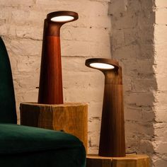 two wooden lamps sitting next to each other in front of a white brick wall and green chair