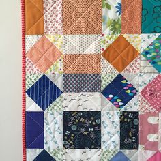 a colorful quilt hanging on the wall next to a white wall with an orange and pink border