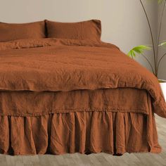 a bed with an orange bedspread and two pillows on top of it, next to a potted plant