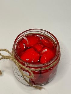 a glass jar filled with red fruit sitting on top of a white table next to a string