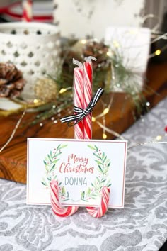 a candy cane with a merry christmas sign on it sitting next to some pine cones