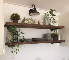 two wooden shelves with plants and dishes on them in the corner of a white kitchen