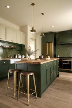 a large kitchen with green cabinets and gold accents on the counter tops, along with two stools