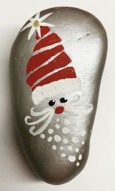 a painted rock with a santa clause hat on it's face and nose, sitting next to a white wall