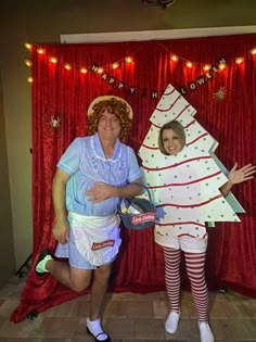 two people dressed up in costumes standing next to each other with christmas decorations on the wall behind them