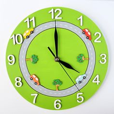 a green clock with cars and trees painted on the face is shown in front of a white background