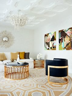 a living room filled with white furniture and paintings on the wall above it's coffee table