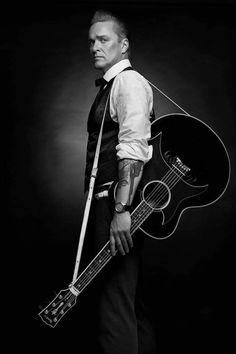 a man holding a guitar in his right hand and wearing a suit on the other