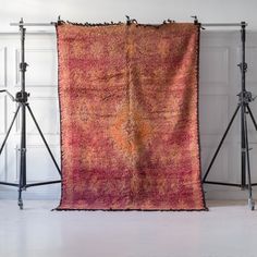 an orange and pink rug is on a tripod in front of a white wall