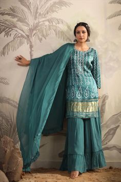 Featuring a teal color kurti in gajji silk base with zari, gota patti, thread, sequins and stones hand embroidery. Printed Kurti with poly crepe lining. It is paired with matching georgette tiered sharara pants with poly crepe lining and a silk chiffon dupatta with fringes for a touch of elegance. Gajji silk kurta, Georgette sharara, Silk chiffon dupatta Lining: Cotton Voile Occasion: Festive Ethnic Motifs Print Pattern Ornamentation: Beads And Stones Kurta Length: 36"-37" Sharara Length: 38" Sl Green Silk Kurta With Dori Work, Designer Green Dola Silk Palazzo Set, Green Slub Silk Anarkali Set With Dori Work, Green Slub Silk Traditional Wear With Dori Work, Bollywood Green Palazzo Set With Dori Work, Festive Green Palazzo Set With Gota Work, Pista Green Silk Palazzo Set For Festivals, Green Dola Silk Palazzo Set With Straight Kurta, Green Palazzo Set With Dori Work And Straight Kurta