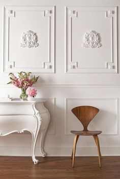 a wooden chair sitting in front of a white table with flowers on top of it