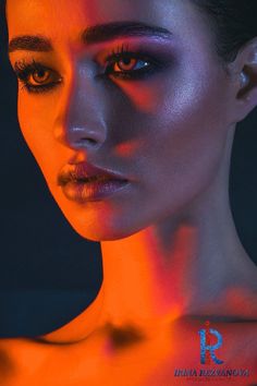 a woman with dark makeup and orange light on her face is looking at the camera