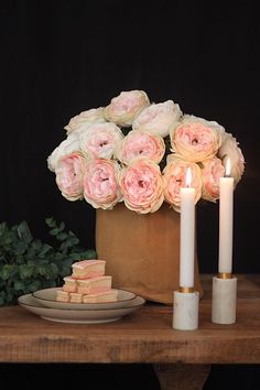 a table topped with candles and flowers next to a bag filled with pink roses on top of a wooden table