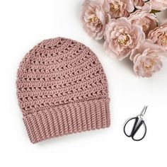 a crocheted hat next to scissors and flowers