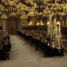 a large group of people sitting in a room with many candles hanging from the ceiling