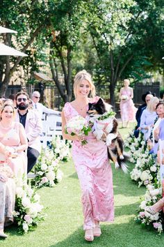 a woman in a pink dress walking down the aisle with a dog on her lap