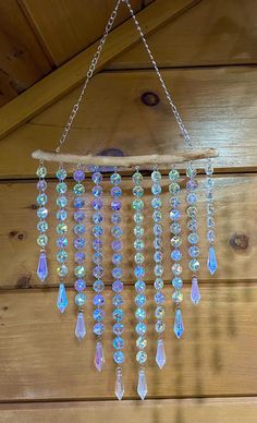 a wind chime hanging from a chain on a wooden wall with beads and chains attached to it