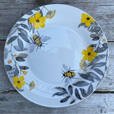 a white plate with yellow flowers and bees painted on the side, sitting on a wooden table