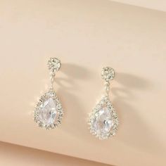 a pair of white earrings with clear stones on the top and bottom, hanging from a beige surface