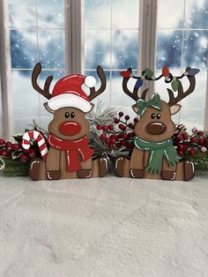 two reindeer figurines sitting next to each other in front of a window with christmas decorations