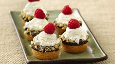 small cupcakes topped with whipped cream and raspberries on a green plate