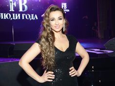 a woman with long hair standing in front of a purple background wearing a black dress