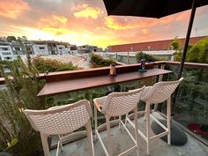 three white chairs and an umbrella on a balcony overlooking the city at sunset or dawn