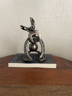 a metal rabbit sculpture sitting on top of a wooden table next to a white wall