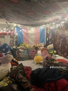 a room filled with lots of stuffed animals on top of blankets and lights hanging from the ceiling