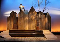 a man standing on top of a wooden bench in front of a tree and fence