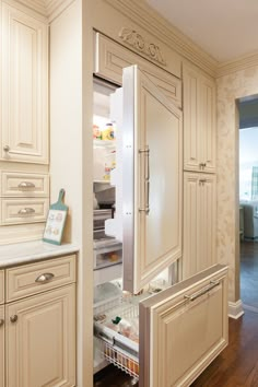 an open refrigerator in a kitchen with wooden floors and white cabinets on both sides is shown