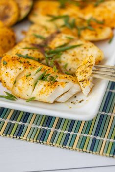 a white plate topped with fish next to potatoes and green garnish on a bamboo mat