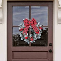 a christmas wreath on the front door of a house with red and white plaid bow