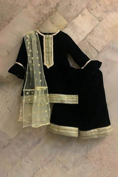 Black velvet kurta with butti embroidered yoke sleeves, and hem.  Comes with palazzo and a gold net dupatta. Pattern: Embroidered Fabric: Velvet, Dupatta : Net Embroidered motifs on dupatta Occasion: Festive & Wedding Care: Dry clean only Fit: Relaxed Velvet Sharara For Navratri Festival, Bollywood Style Velvet Sharara For Navratri, Traditional Velvet Sharara For Navratri, Velvet Sharara With Zari Work For Navratri, Anarkali Velvet Sharara For Navratri, Navratri Velvet Sharara With Zari Work, Velvet Traditional Wear For Diwali, Gold Long Sleeve Lehenga With Gota Work, Velvet Sharara With Resham Embroidery For Navratri