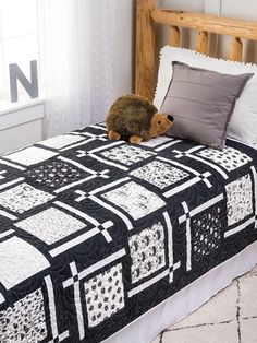 a teddy bear sitting on top of a black and white quilted bedspread