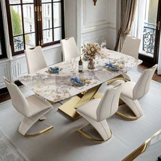 a dining room table with white chairs and gold trimmings on the top, in front of large windows